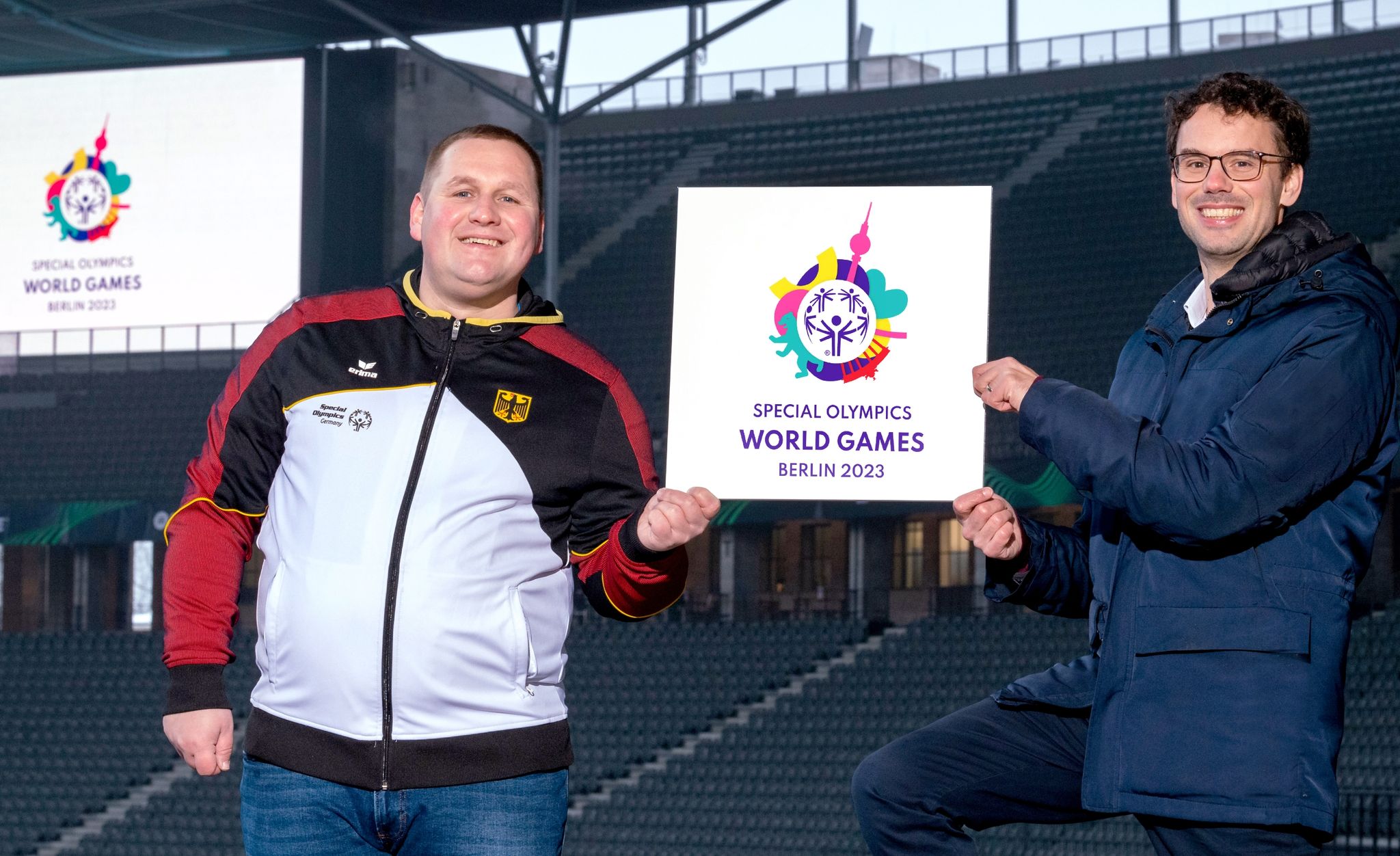 Dennis Mellentin (l), Athletensprecher Special Olympics Berlin, und Sven Albrecht, CEO des OK der Special Olympics World Games Berlin 2023 mit dem Logo der Weltspiele 2023.