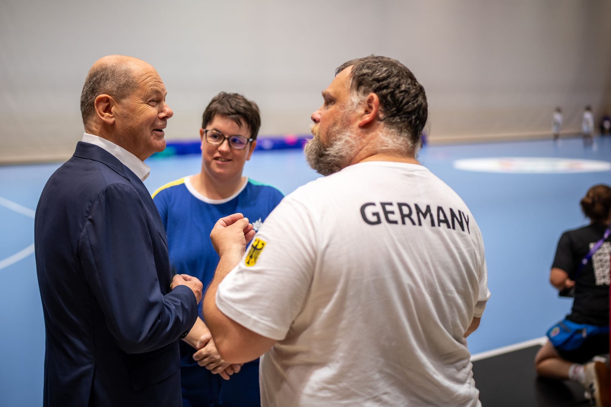 Bundeskanzler Olaf Scholz (SPD, l), unterhält sich bei seinem Besuch der Handball Wettbewerbe mit Athleten und Trainern.